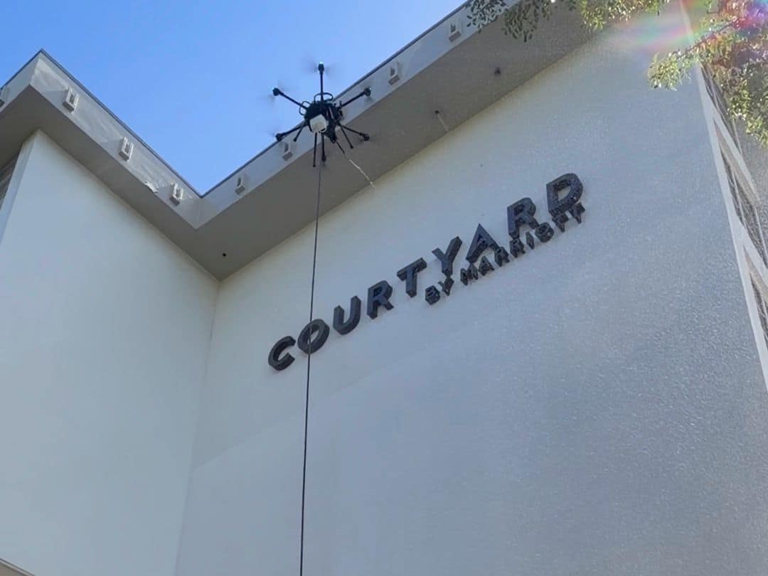 The tethered cleaning drone washing the facade beside the Courtyard by Marriott sign in Coral Gables